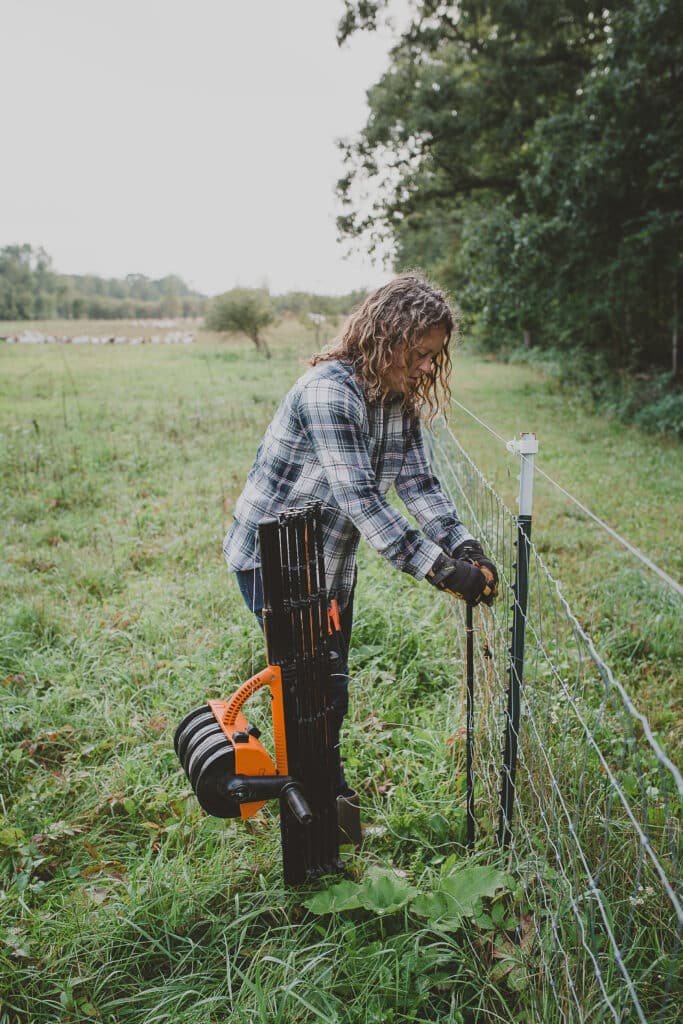 Leslie in a field fixing a portion of electric fence.